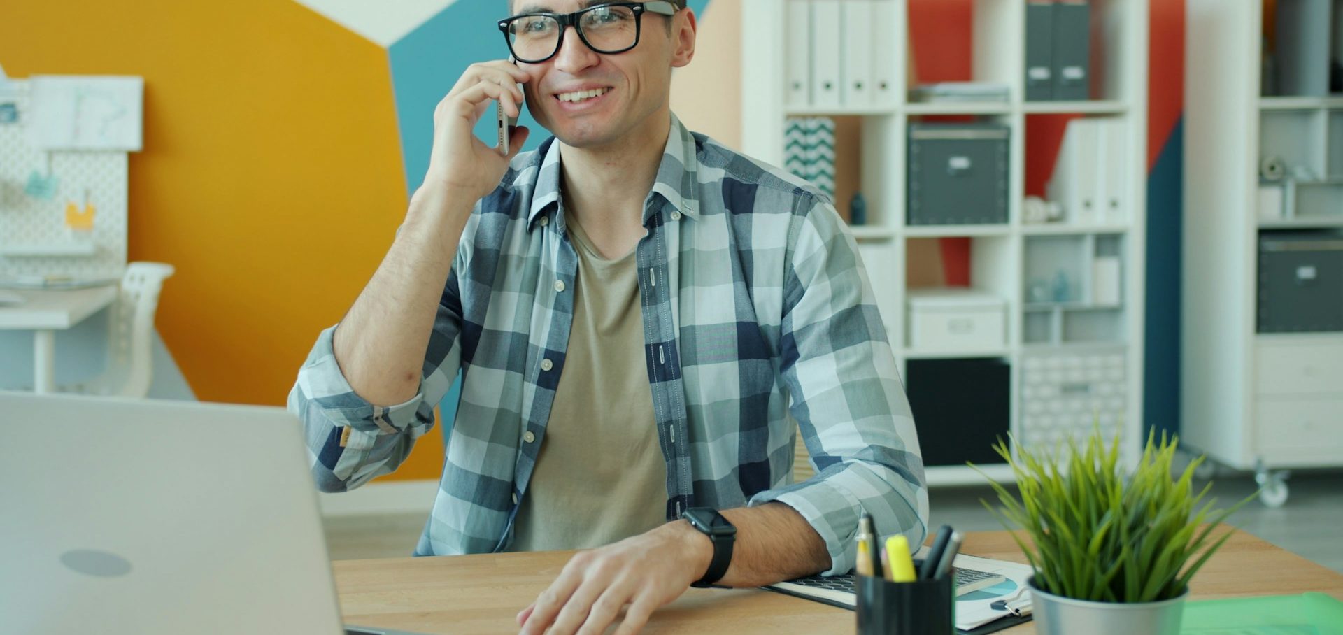 Hombre llamando por teléfono mientras trabaja en una computadora portátil en una oficina moderna.