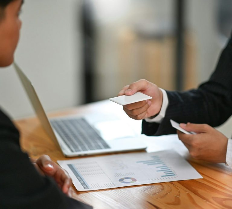 Dos personas en una reunión, intercambiando tarjetas de presentación y analizando gráficos.