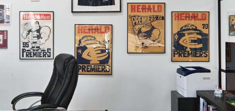 Pared con carteles vintage y silla de oficina, junto a una impresora.